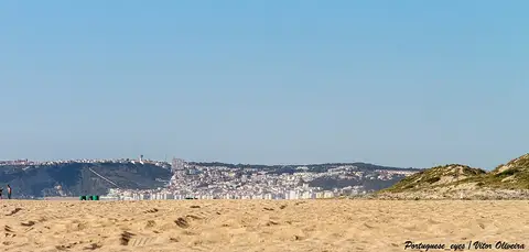 Areal extenso da Praia do Salgado com a Nazaré ao fundo, sob céu azul limpo