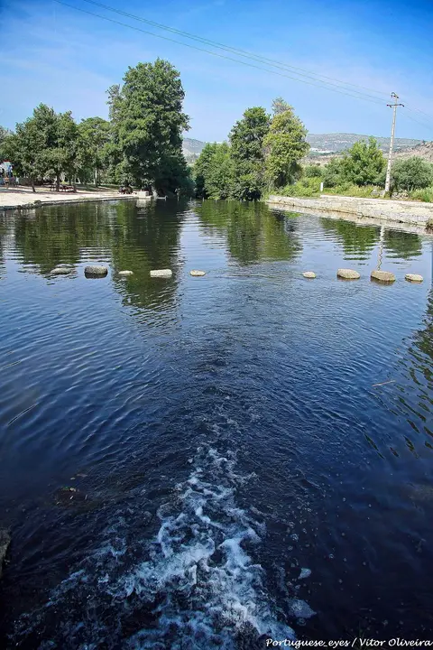 Praia fluvial do Mondego com passadeira de pedras sobre a água e árvores nas margens