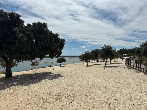 Praia fluvial de areia com azinheiras, balizas e passadiço junto à albufeira, em Albergaria dos Fusos