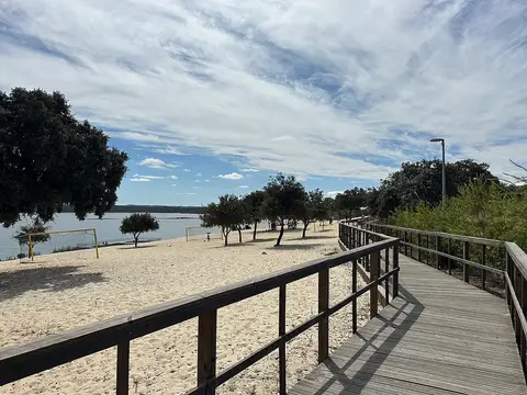 Passadiço de madeira junto à praia fluvial de Albergaria dos Fusos, com areia, árvores e albufeira.