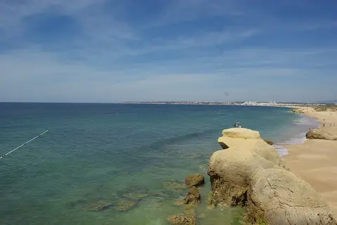 Praia da Galé em Albufeira, com rochas douradas, areal extenso e mar azul-turquesa.