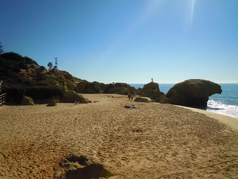 Praia da Galé com areal amplo, formações rochosas douradas e mar calmo sob céu azul