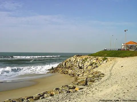 Praia de Cortegaça com areal, rochas de proteção, ondas e apoio de praia ao fundo