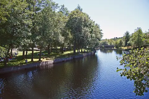 Praia fluvial de Segões com margem relvada arborizada junto ao rio calmo