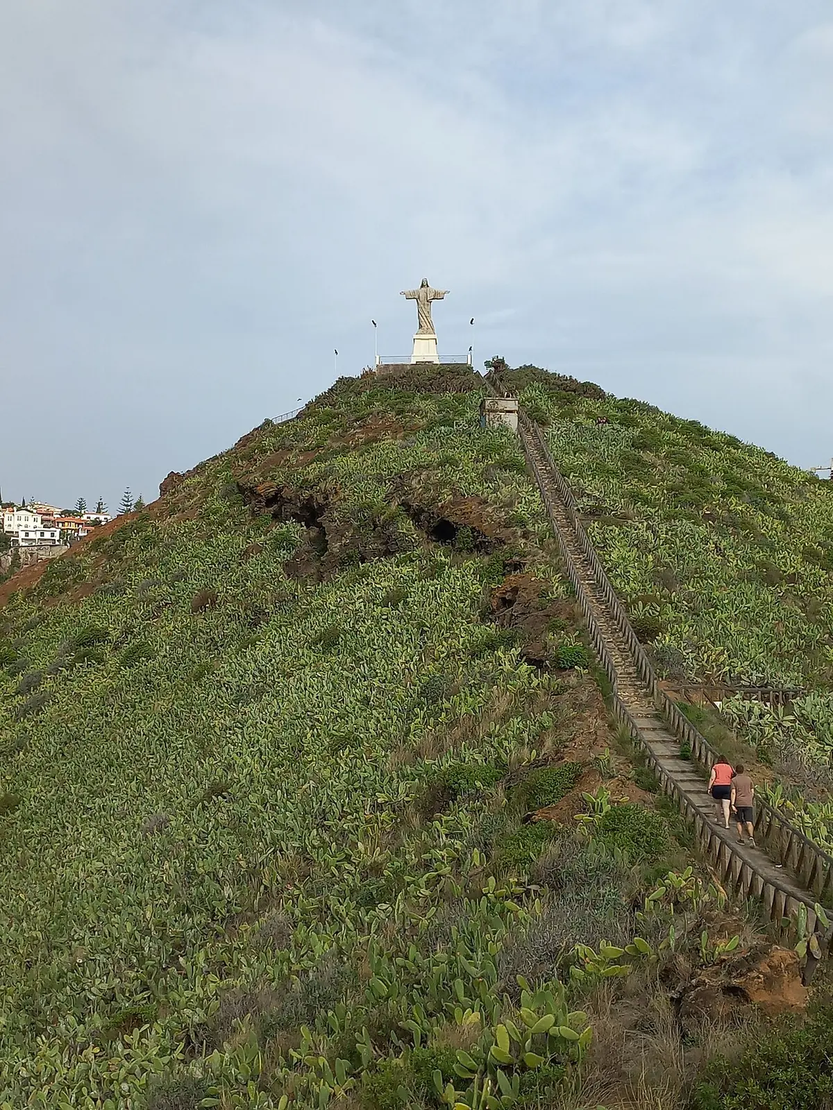 Estátua do Cristo Rei no topo da colina verde da Ponta do Garajau, com escadaria a subir a encosta