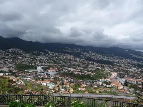 Vista do Funchal a partir do miradouro do Pico dos Barcelos, com encostas urbanizadas e céu nublado