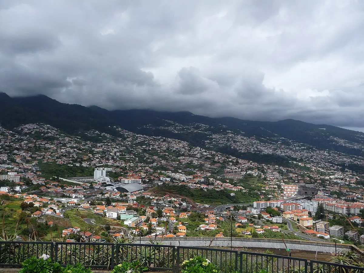 Vista do Funchal a partir do miradouro do Pico dos Barcelos, com encostas urbanizadas e céu nublado