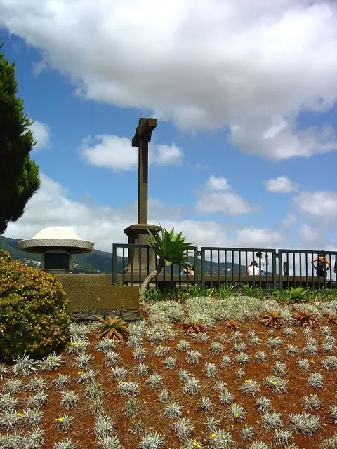 Miradouro do Pico dos Barcelos com cruzeiro de pedra, canteiro florido e vista das montanhas do Funchal