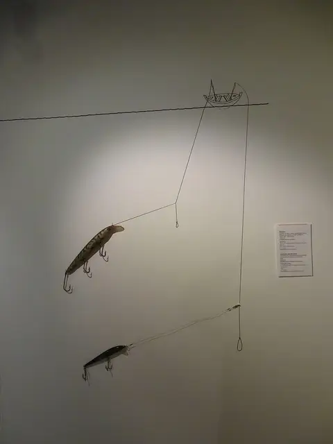 Exposição museológica com iscos de pesca e linhas montados numa parede clara