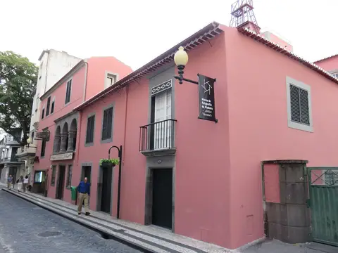 Fachada rosa do Museu da Fotografia "Vicentes" no Funchal, com letreiro na rua em calçada.