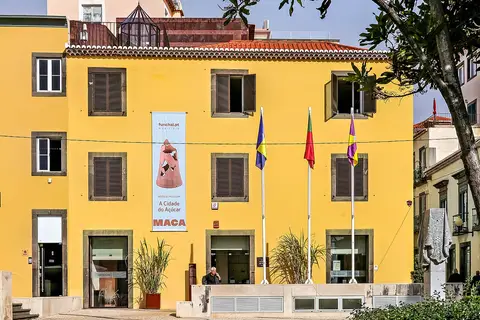 Fachada amarela do Núcleu Museológico A Cidade do Açúcar, no Funchal, com bandeiras e cartaz do museu.
