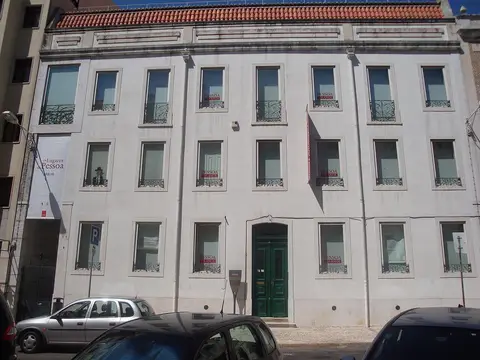 Fachada branca da Casa Fernando Pessoa, em Lisboa, com porta verde e cartazes nas janelas