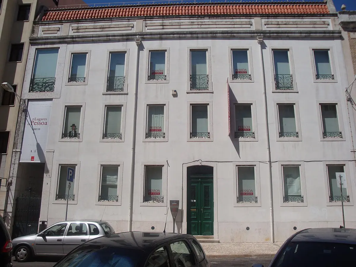 Fachada branca da Casa Fernando Pessoa, em Lisboa, com porta verde e cartazes nas janelas