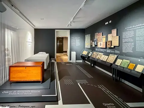 Sala do quarto de Fernando Pessoa na Casa Fernando Pessoa, com cama, arca de madeira e vitrinas com publicações.