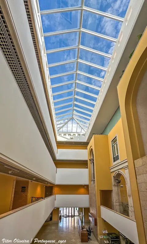 Átrio interior do Museu da Farmácia em Lisboa com grande clarabóia de vidro e paredes amarelas.