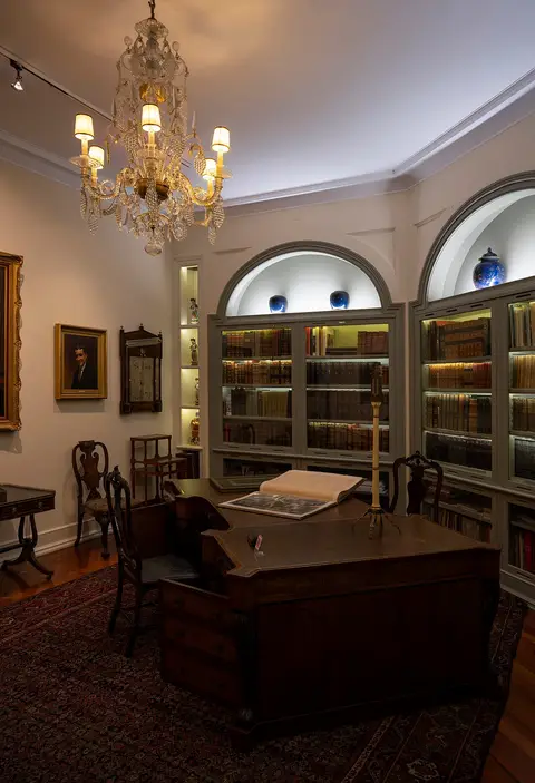 Sala de escritório do Museu Medeiros e Almeida com secretária, lustre de cristal e estantes de livros