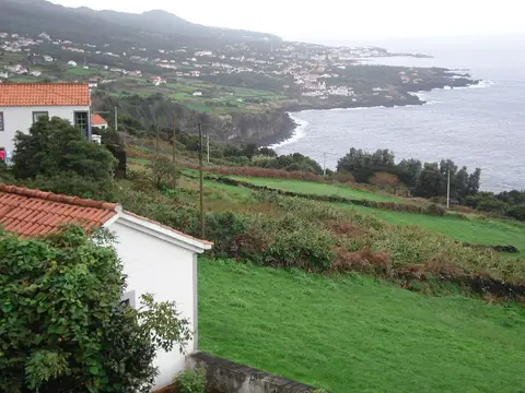 Vista da costa com casas brancas de telhado vermelho e pastagens verdes junto ao mar, nos Açores