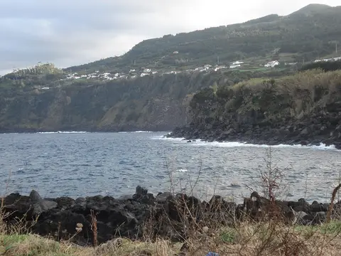 Vista da costa rochosa e falésias com casas dispersas na encosta, junto ao mar nos Açores