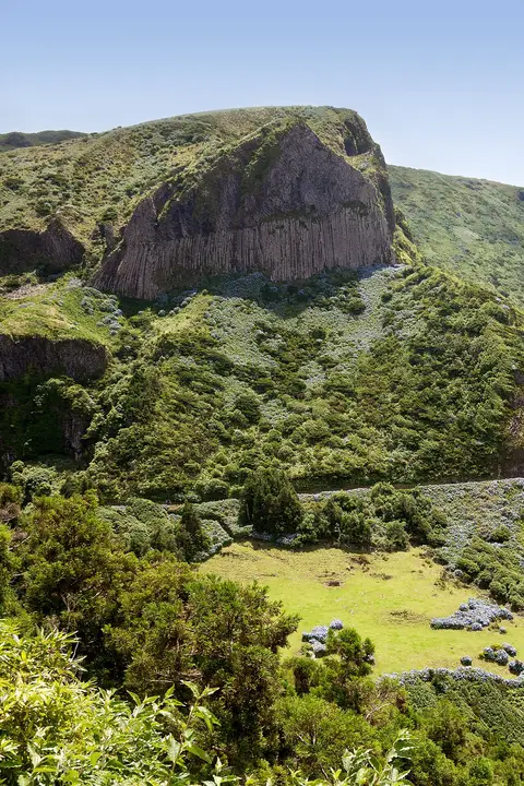 Rocha dos Bordões, formação de colunas basálticas rodeada de vegetação verde, na ilha das Flores