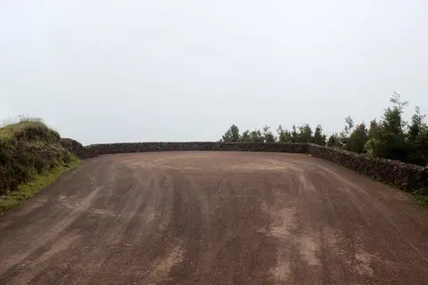 Explanada de terra batida do Miradouro do Pico do Paúl, com muro de pedra e céu nublado