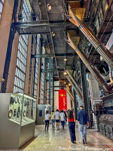 Sala das caldeiras da Central Tejo, com estruturas metálicas, tubagens e visitantes a percorrer o espaço.