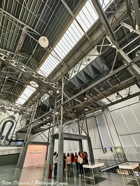 Interior industrial da Central Tejo no MAAT, com estruturas metálicas e grupo de visitantes ao fundo