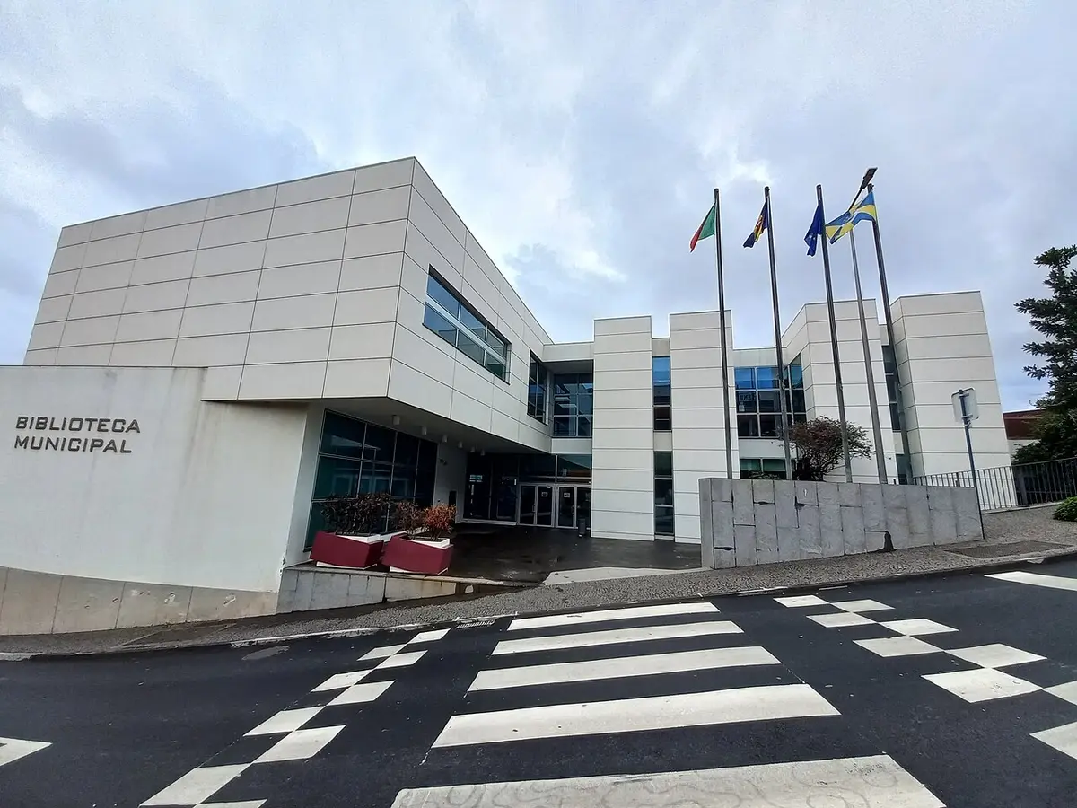 Fachada moderna da Biblioteca Municipal de Câmara de Lobos com bandeiras e passadeira em primeiro plano