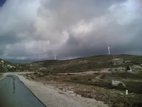 Estrada na Serra do Barroso com aerogeradores ao fundo e céu carregado de nuvens