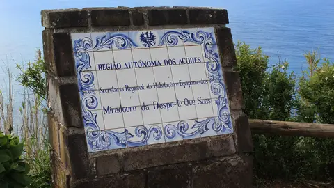 Painel de azulejos em pedra com o nome do Miradouro da Despe-te que Suas, com o mar ao fundo