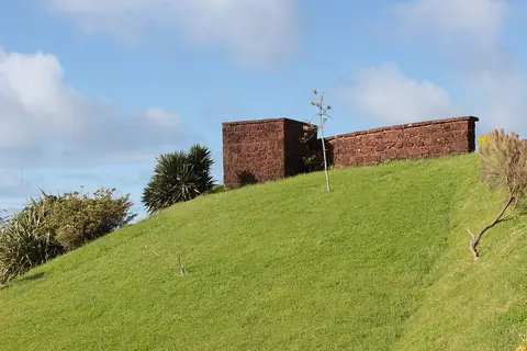 Muro de pedra vermelha do miradouro no topo de uma encosta relvada, sob céu azul