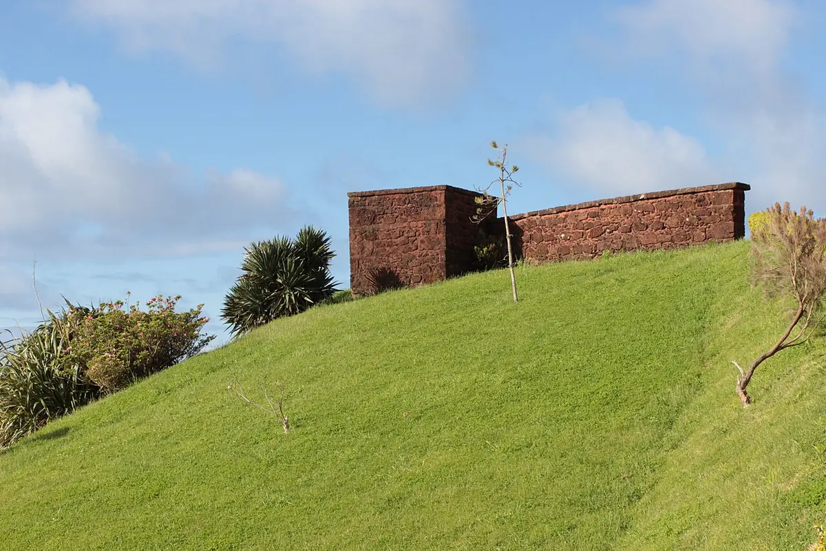 Muro de pedra vermelha do miradouro no topo de uma encosta relvada, sob céu azul