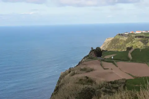 Vista do miradouro sobre falésias verdes, campos cultivados e oceano Atlântico