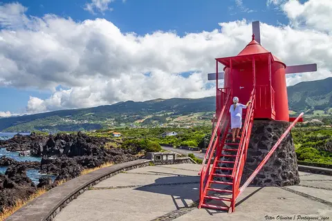 Moinho vermelho junto à costa em São Roque do Pico, com escadas e vista para o mar e montanhas.