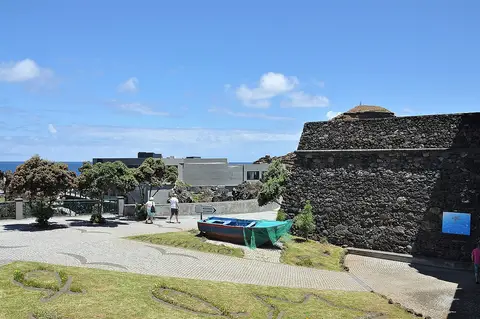Forte de pedra que alberga o Aquário da Madeira, com barco de pesca e calçada em frente