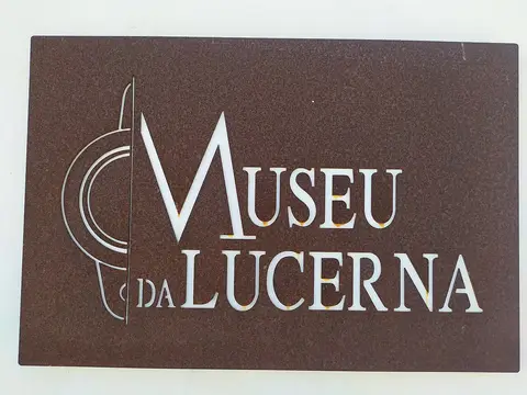 Placa metálica castanha com a inscrição "Museu da Lucerna" em parede branca