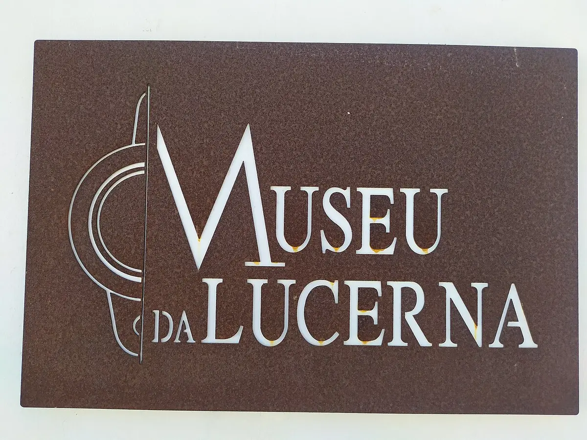 Placa metálica castanha com a inscrição "Museu da Lucerna" em parede branca