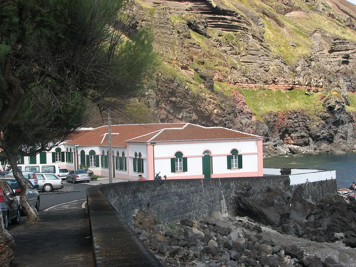 Edifício branco e rosa das Termas do Carapacho junto ao mar, com falésia ao fundo, na Graciosa