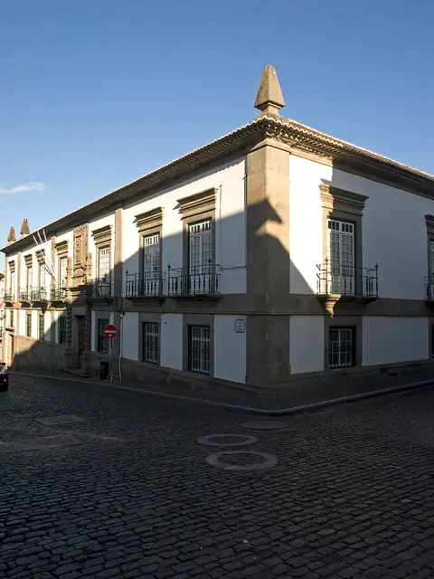 Fachada em esquina do Palácio Bettencourt, edifício branco com cantarias e varandas de ferro, sobre rua empedrada