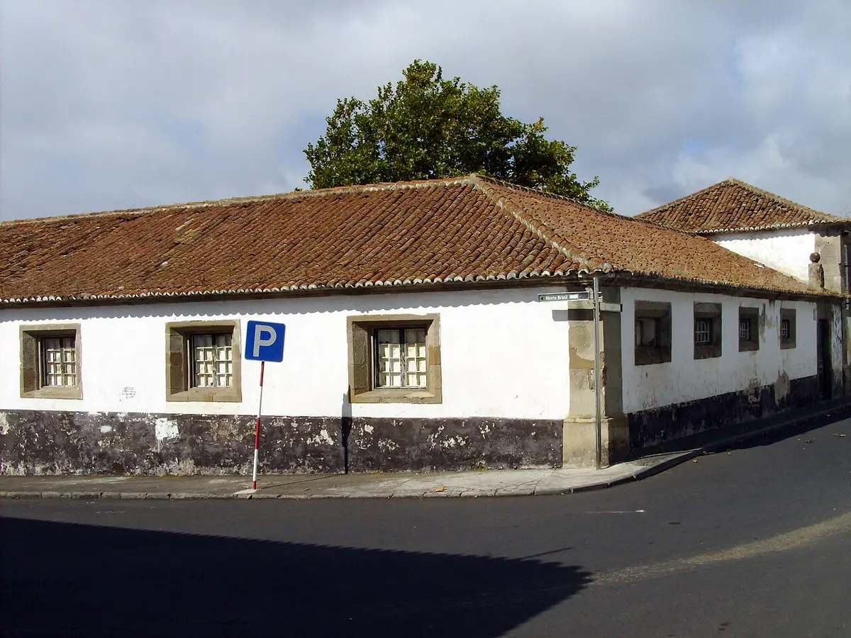 Edifício histórico caiado de branco com telhado de telha, na esquina de uma rua