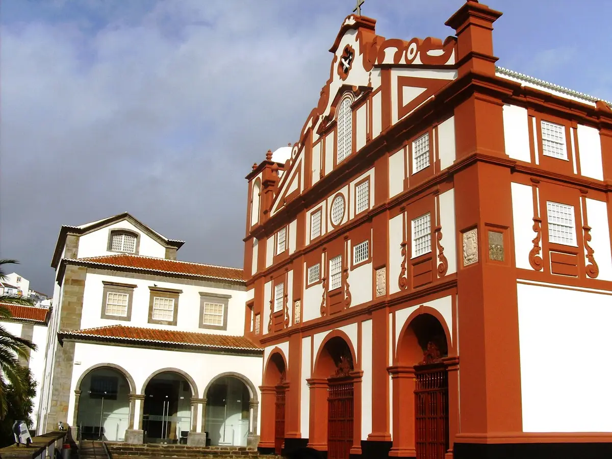 Fachada vermelha e branca do Museu de Angra do Heroísmo, nos Açores, com arcadas e frontão barroco