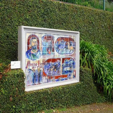 Painel de azulejos sobre Afonso Henriques numa parede coberta de vegetação, no Monte Palace