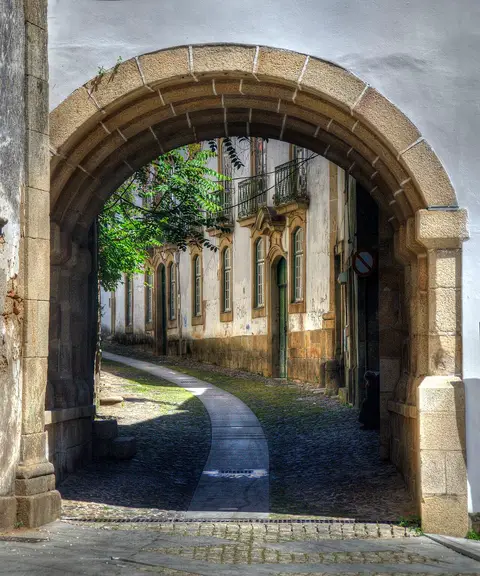Arco de pedra do Arco do Bispo com vista para uma rua calcetada e casas antigas