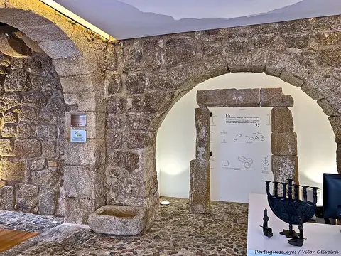 Interior em pedra com arcos de granito, painel expositivo e candelabro, em espaço museológico