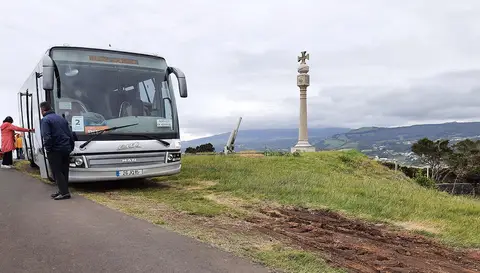 Miradouro do Pico das Cruzinhas com monumento em cruz de pedra e autocarro turístico estacionado