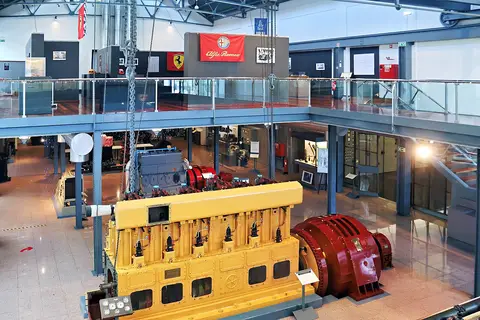 Interior do Museu da Electricidade com grande motor amarelo e gerador vermelho em exposição