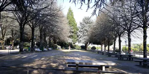 Parque arborizado com mesas de merendas em pedra e bancos, com zona de sombra sob as árvores