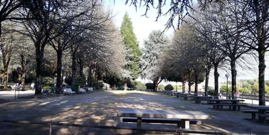 Parque arborizado com mesas de merendas em pedra e bancos, com zona de sombra sob as árvores