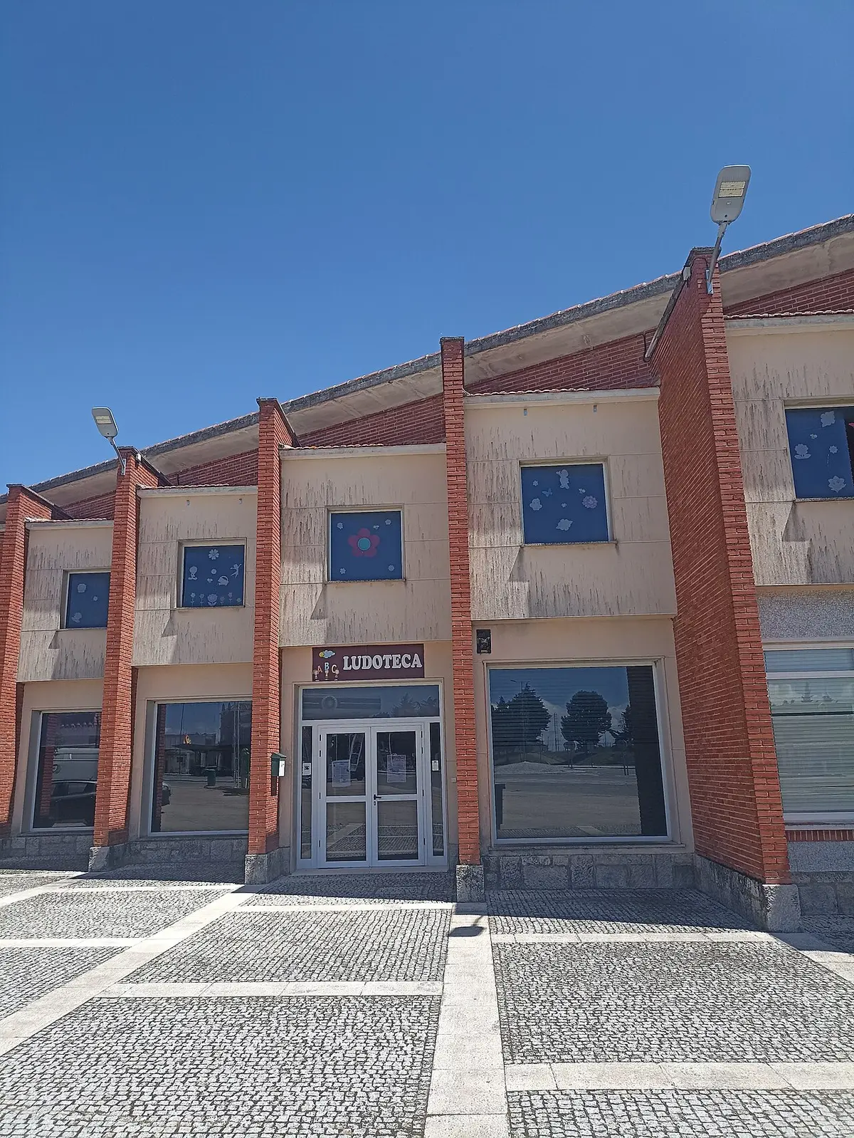 Fachada de edifício com letreiro "Ludoteca", janelas decoradas e calçada em frente