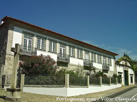 Casa senhorial de granito e fachada branca com varandas de ferro forjado, em Travassos