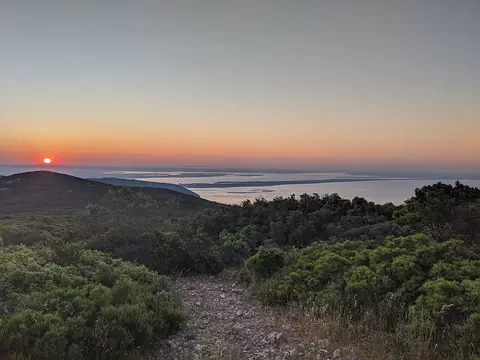 Vista do alto do Formosinho ao pôr do sol, com vegetação baixa, trilho pedregoso e mar ao fundo